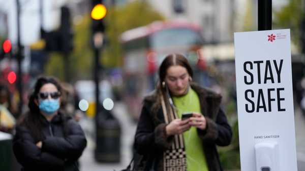 Bus passengers wait at a bus stop next to a Stay Safe sign which encourages social distancing and the wearing of masks to curb the spread of COVID-19, in London, Tuesday, Nov. 30, 2021.