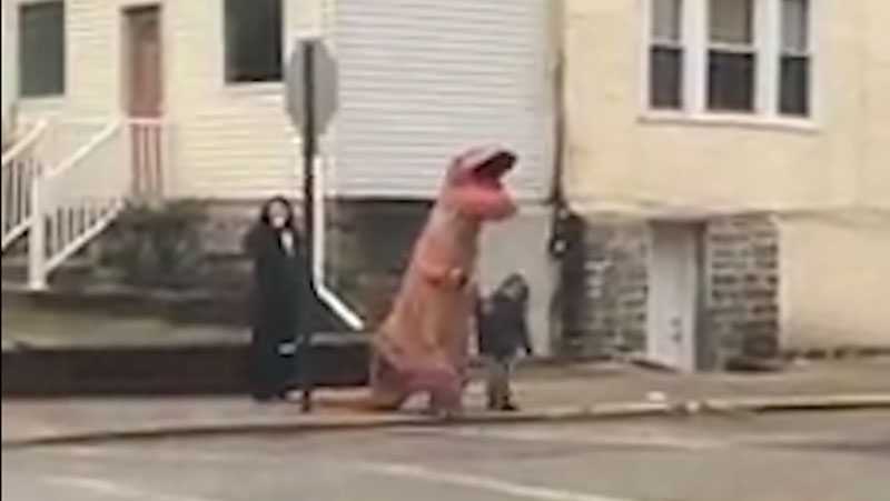 A person in a dinosaur costume walks a child to school
