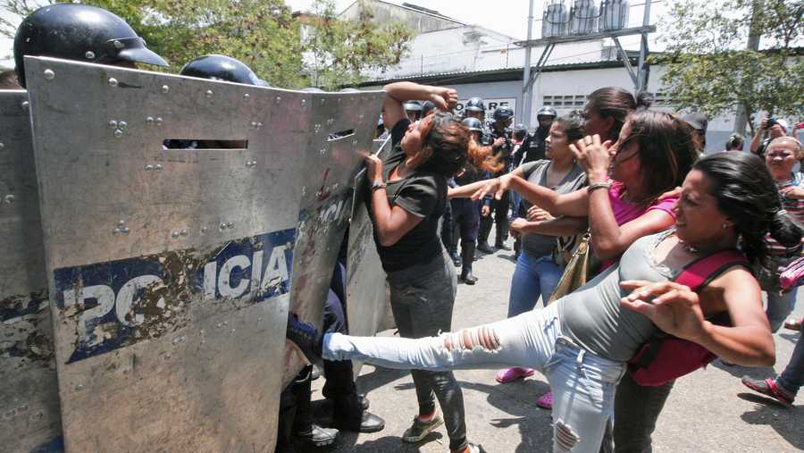 A woman kicks at a riot police shield as relatives of prisoners wait to hear news about their family members imprisoned at a police station where a riot broke out, in Valencia, Venezuela, Wednesday, March 28, 2018.