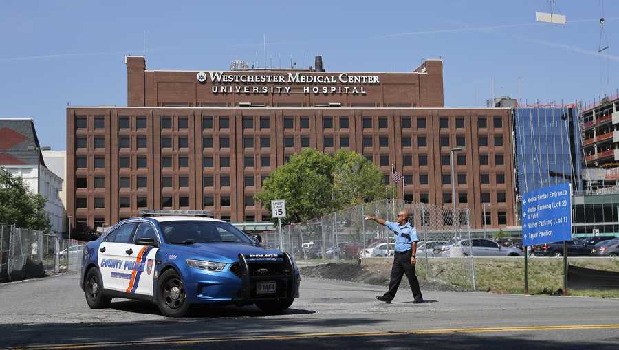 A Westchester Medical Center security guard directs traffic as a Westchester County police car pulls out of the drive to the main entrance of the hospital, Wednesday, Aug. 8, 2018, in Valhalla, N.Y. A man shot a female patient and then killed himself at the suburban New York hospital Wednesday, police said.