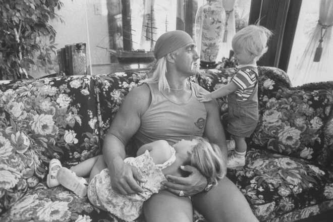 Wrestler Hulk Hogan cuddling w. his 3-yr-old daughter Brooke as he chats w. his 1-yr-old son Nicholas while relaxing together on a floral print couch at home.  (Photo by Acey Harper/Getty Images)