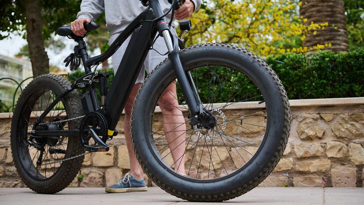 A modern ecologically friendly e-bike in the city, ready for rent. Cropped view of a sporty man riding electric motor bike. Bike sharing city service. Environmental conservation. Sustainable lifestyle