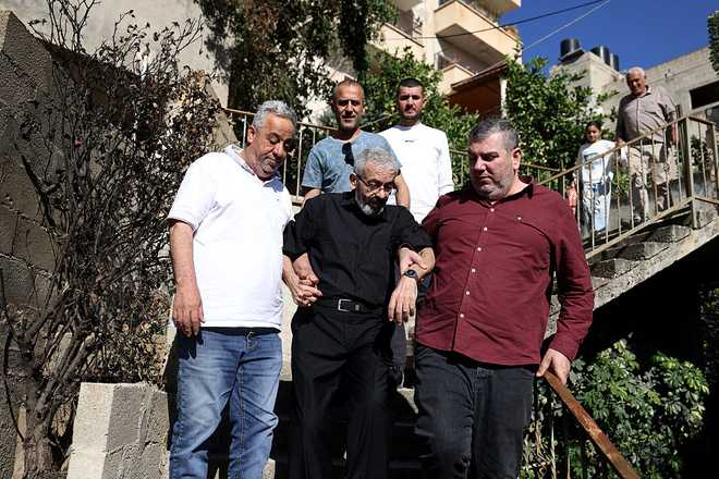 Palestinian journalist Ali al-Samoudi (C) is helped down the stairs at his home in the northern city of Jenin, in the Israeli-occupied Palestinian West Bank on May 1, 2026. Sixty-year-old Al-Samoudi was released following one-year in detention in the Israeli Naqab Prison, located in southern Israel. He was released and checked at the Jenin Hospital where he said, "I was 120 kilogrammes; my weight now is barely 60 kilogrammes". Israel has jailed an increasing number of journalists since 2023, the year of Hamas's unprecedented October 7 attack on Israel, which responded with a devastating war in the Gaza Strip. (Photo by JAAFAR ASHTIYEH / AFP via Getty Images)