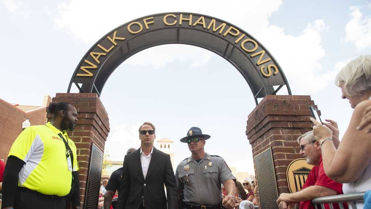 Photo: WDSU Lane Kiffin flocked by an MHP officer when he was head coach at Ole Miss ahead of an LSU game