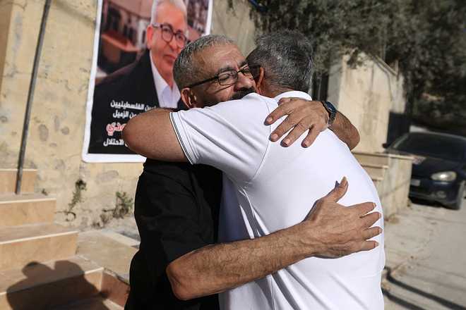 Palestinian journalist Ali al-Samoudi is hugged by a relative as he stands in front of a large image of himself taken before he was detained by the Israeli army and held for a year, at his home in the northern city of Jenin, in the Israeli-occupied Palestinian West Bank on May 1, 2026. Sixty-year-old Al-Samoudi was released following one-year in detention in the Israeli Naqab Prison, located in southern Israel. He was released and checked at the Jenin Hospital where he said, "I was 120 kilogrammes; my weight now is barely 60 kilogrammes". Israel has jailed an increasing number of journalists since 2023, the year of Hamas's unprecedented October 7 attack on Israel, which responded with a devastating war in the Gaza Strip. (Photo by JAAFAR ASHTIYEH / AFP via Getty Images)