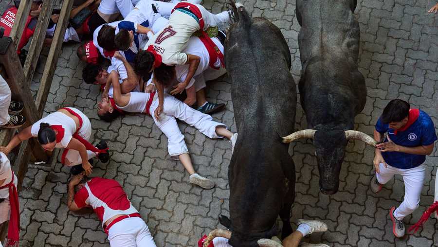 Revelers fall next to Jose Escolar's fighting bulls during the fifth running of the bulls at the San Ferm&iacute;n festival in Pamplona, Spain, Saturday, July 11, 2026.