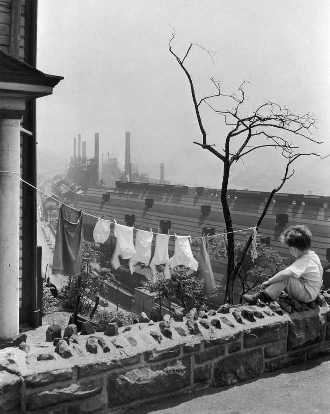 circa 1935:  A young boy sits on a balcony overlooking a clothesline and a steel mill, Pittsburgh, Pennsylvania, 1930s.  (Photo by Newman-Schmidt Studios/Getty Images)
