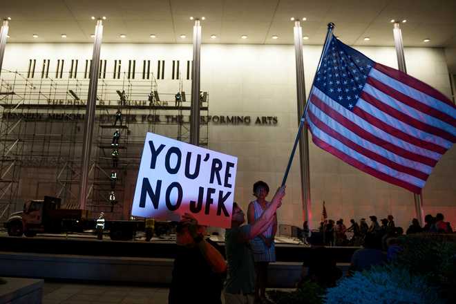 Protestors wave a U.S. and signs as workers prepare to remove President Donald Trump&amp;#39;s name from the John F. Kennedy Center for the Performing Arts in Washington, Saturday, June 13, 2026. (AP Photo/Cliff Owen)
