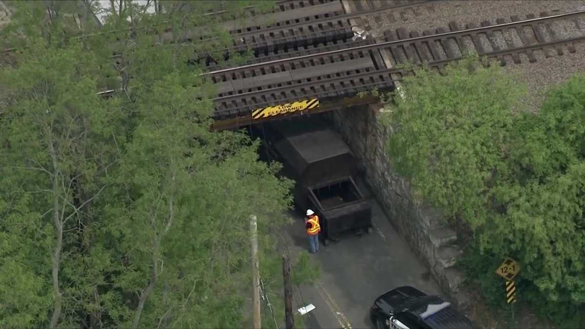Truck hauling trash compactor strikes Mass. rail bridge