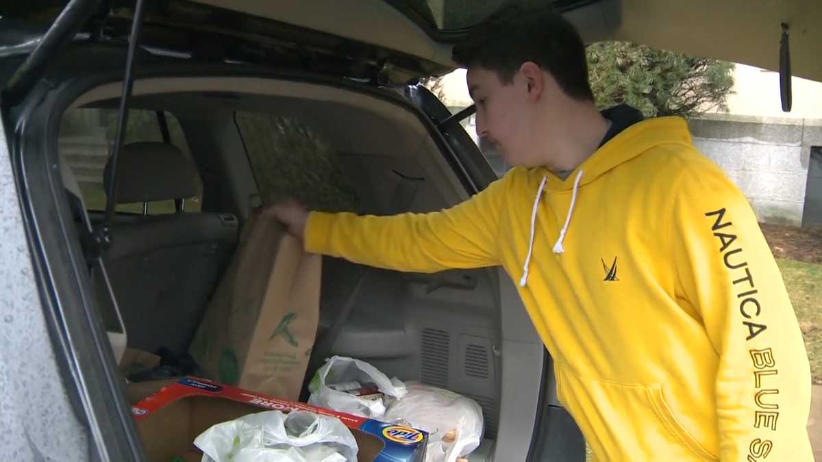 Young man in yellow hoodie putting groceries in the back of his car